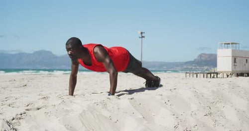Focused african american man doing press ups on the beach, exercising outdoors by the sea