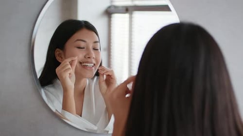 Glückliche Chinesin, die im Badezimmer Zähne mit Zahnseide mit Zahnseide verwendet