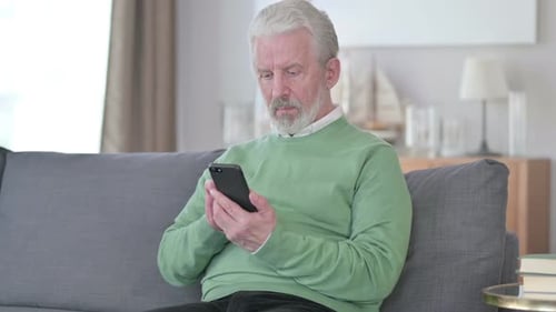 Senior Man Using Smartphone on Gray Sofa