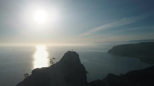 Aerial Silhouette of a Young Woman Standing on the Top of a Mountain Facing the Sea. Lady on the