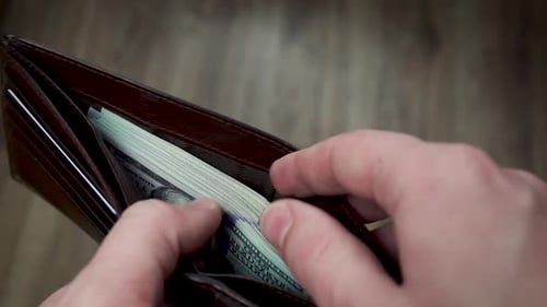 Hands remove stack of cash from brown wallet