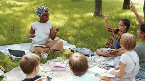 Black Female Teacher Giving Lesson to Group of Kids in Park