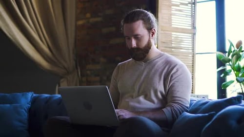 Relaxed Serious Hipster Guy Student Freelancer Using Laptop Device Sit on Sofa at Home Office Spbd