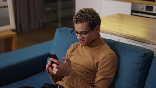 Young Adult Using Phone on Blue Couch Indoors