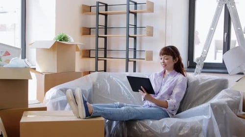 Woman Relaxes on Sofa with Tablet After Moving