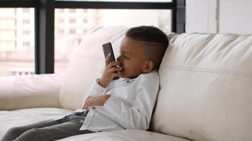 Smiling Child Chatting on Smartphone on White Sofa