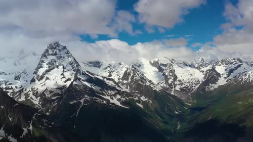 Air Flight Through Mountain Clouds Over Beautiful Snowcapped Peaks of Mountains and Glaciers