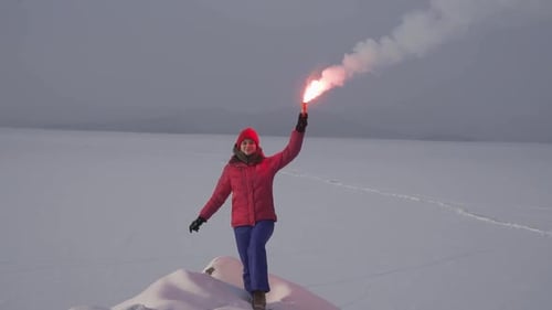Woman Signals on Snowy Hilltop with a Flare