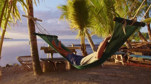 Young Woman Wearing a Sitting in the Sun and Swinging in a Hammock While Looking Out at the Ocean