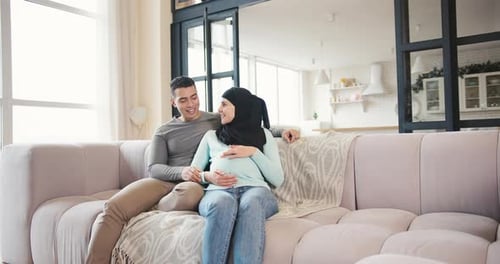 Loving Couple Sitting on Couch Expecting a Baby