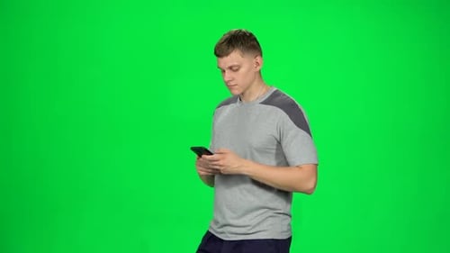 Smiling Man Goes and Texting with Smartphone on Green Screen at Studio. Slow Motion