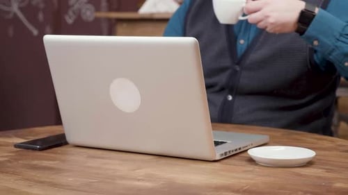 Male Freelancer Sips Coffee While Working From a Small Coffee Shop.