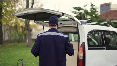 Hübscher Kurier, der das Kartonpaket in den Lieferwagen legt und das Paket einschreibt