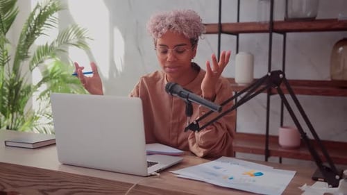 Woman Talking at Laptop with Microphone at Desk