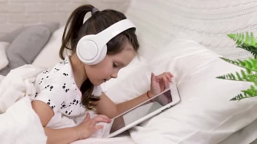 Girl Lying in Bed Using Tablet with Headphones