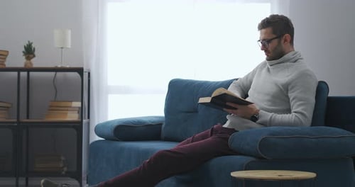 Man Reading Book on Couch Indoors