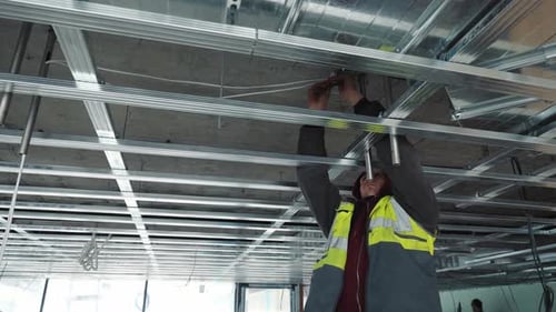 Construction Worker Connects Wiring on Building Ceiling