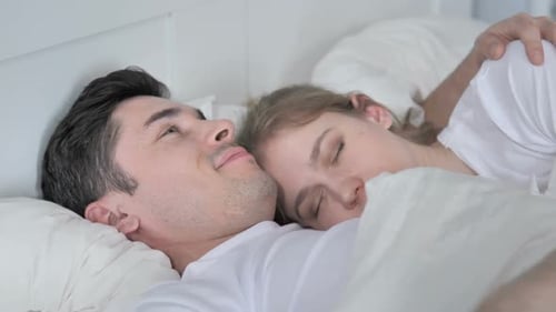 Hombre besa a novia durmiendo en la cama abrazándose