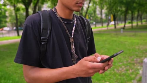 Young Adult Uses Smartphone in Green Urban Park