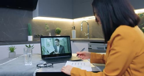 Femme assise dans la cuisine et écoutant expliquer par son partenaire par vidéoconférence