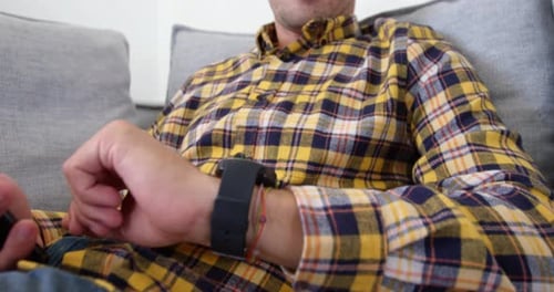 Man Relaxing on Couch Using Smartphone and Smartwatch