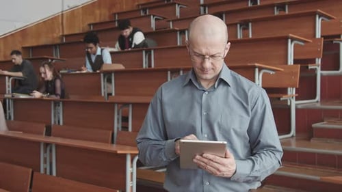 Professor with Tablet Posing for Camera in Lecture Hall with Students