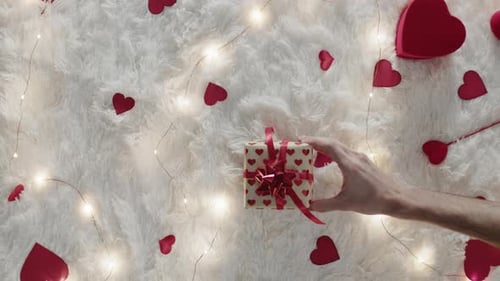 Hand Placing Wrapped Gift With Hearts and Lights