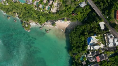 Vista aérea de arriba hacia abajo de lujosos complejos turísticos tropicales en un acantilado sobre una playa de arena en Bali