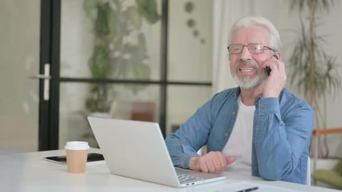 Senior Man Using Phone and Laptop at Desk