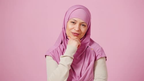 Nachdenkliche islamische Frau mittleren Alters, die mit Bewertung und Zeigen in die Kamera blickt, bekam Rosa