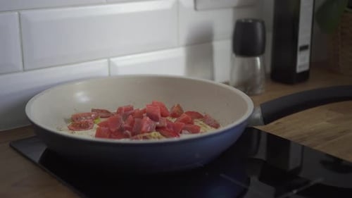 Adding Chopped Tomatoes to Eggs in Frying Pan