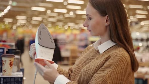 Young Woman Buys a Steam Iron in a Store