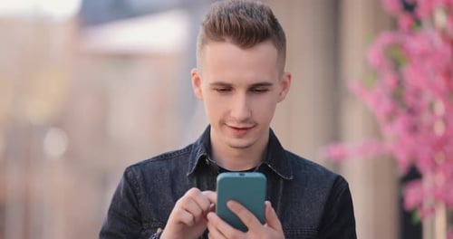 Young Smiling Man Using Mobile Phone in a Spring City