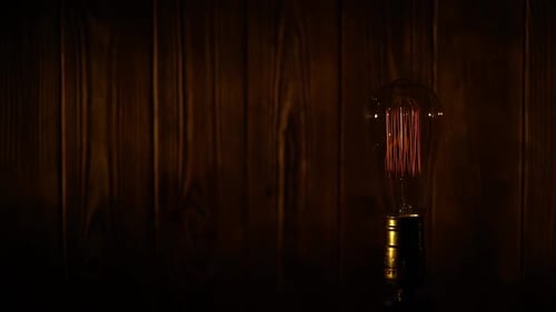 Old Vintage Edison Light Bulb Glowing on Background of Wooden Planks