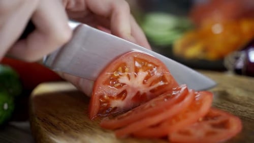 Hand Slices Tomato on Cutting Board