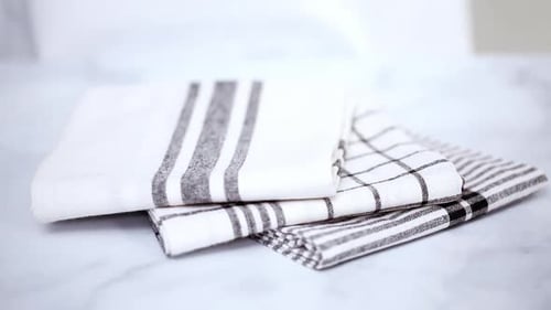 Hand stacking folded white kitchen towels on counter