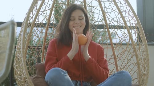 Young Woman Tosses Orange in Wicker Chair