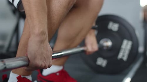 Closeup of hands of athletic man grabbing and lifting barbell at gym. Male bodybuilder lifts barbell