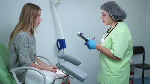 Side View Teenage Caucasian Girl Sitting on Gynecological Chair Listening to Young Doctor Talking