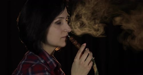 Woman Exhaling Hookah Smoke Against Dark Background