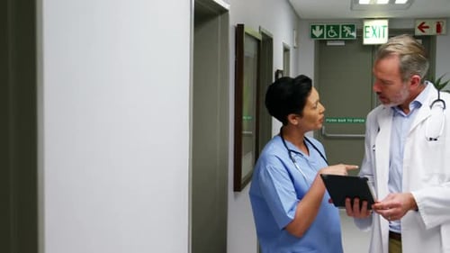 Doctors Discussing Information on Tablet in Hospital Hallway