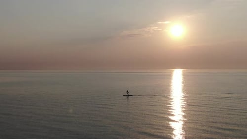 Man paddleboarding at the sea during sunset - aerial view