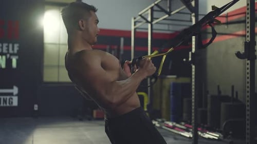 Asian active athlete man straight out his arms to hold TRX anchored to a steel beam in stadium.