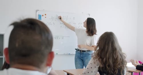 Female Teacher Writing Mathematical Formulas on White Board in a School Classroom