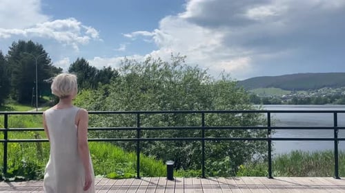A Beautiful Young Girl Approaches the Railing in the Park By the Lake