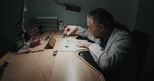 A watchmaker carefully removing the parts of a wristwatch he's repairing - wide shot