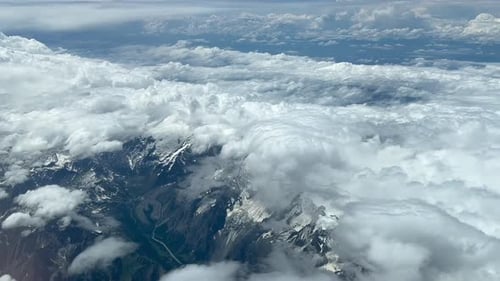 Breathtaking mountain range covered by cumulus clouds. Pov above view from airplane window