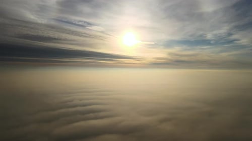 Aerial view of bright yellow sunset over white dense clouds with blue sky overhead.