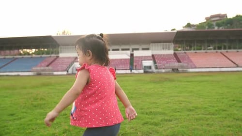 Asiatisches kleines Mädchen läuft auf dem Rasen im Stadion