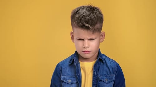 Retrato de primer plano de un niño triste con el ceño fruncido pensando en la resolución de problemas posando aislado en naranja